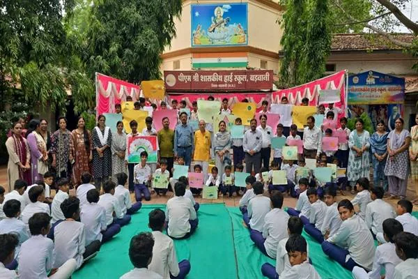 स्कूल परिसर में चित्र लिए खड़े विद्यार्थी और शिक्षक, सामने हरी चटाई पर बैठे स्कूली बच्चे