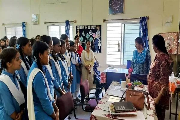 कमरे में नीली-सफेद वर्दी पहने छात्राएं खड़ी हैं और सामने दो महिलाएं मेज के पास उनसे बात कर रही हैं