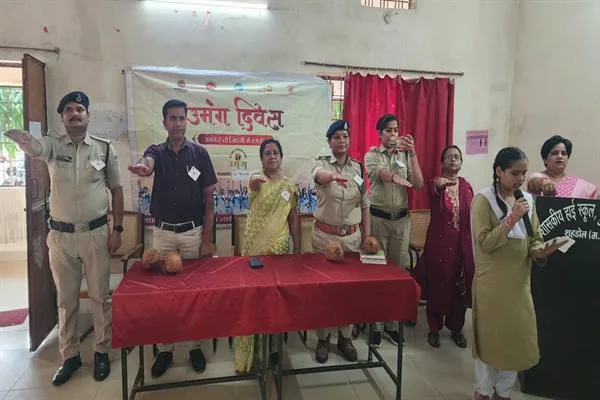 स्कूल के एक कक्ष में पुलिसकर्मी, शिक्षक और विद्यार्थी मंच के सामने हाथ आगे बढ़ाए खड़े हैं, एक छात्रा माइक से बोल रही है और पीछे उमंग दिवस का बैनर लगा है।
